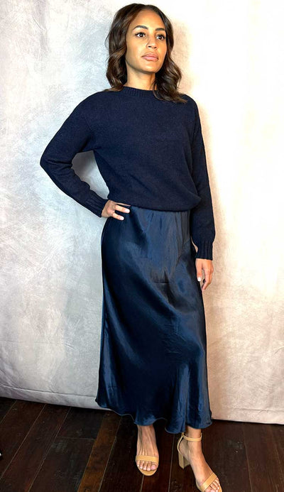 Woman wearing a navy blue sweater and skirt against a neutral background