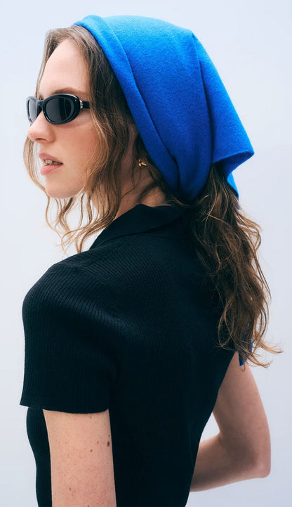 Woman wearing a white and warren cashmere neckerchief mini scarf in bright cobalt blue - wearing it on her head like a babushka on a white background