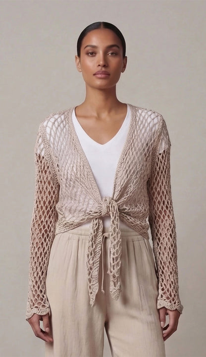 Woman wearing a taupe open crochet top over a white top and beige pants on a plain background