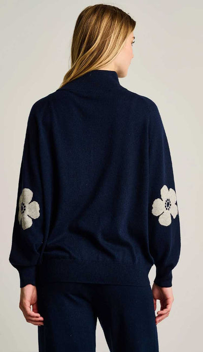 Navy blue sweater with white floral poppy  patterns on sleeves worn by a person against a plain background