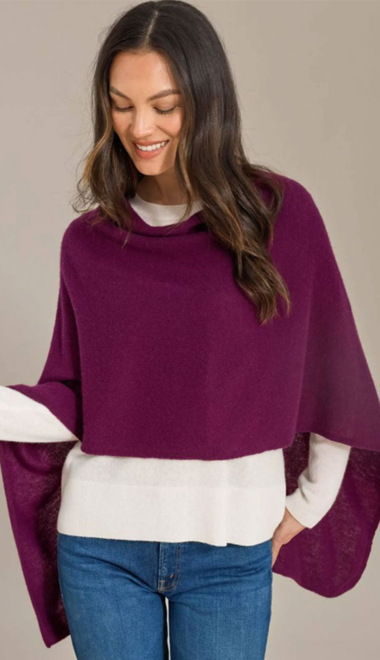 Woman wearing a regal alashan cashmere dress topper poncho over a white shirt and blue jeans on a beige background