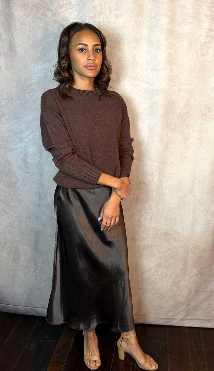 Woman wearing a brown sweater and dark  brown satin skirt against a neutral background