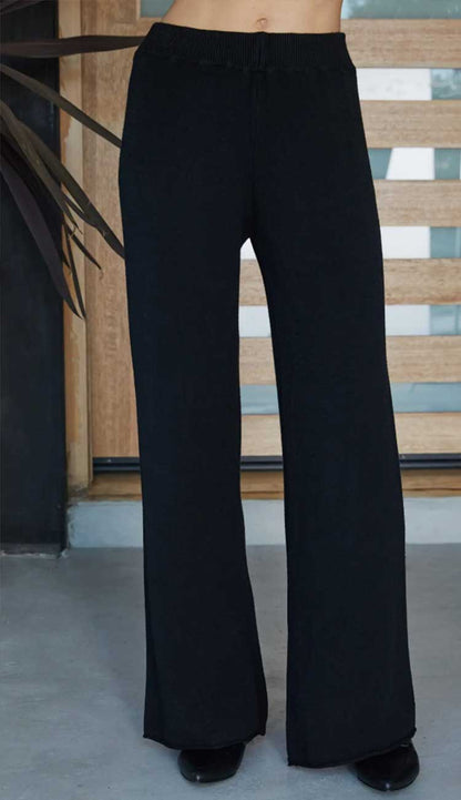 Black wide-leg pants worn by a person against a wooden panel background