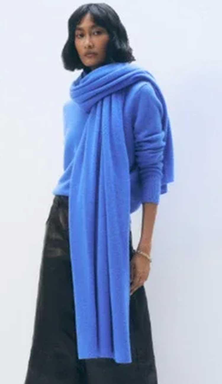 woman wearing a blue travel wrap and sweater with leather pants on a white bakcground