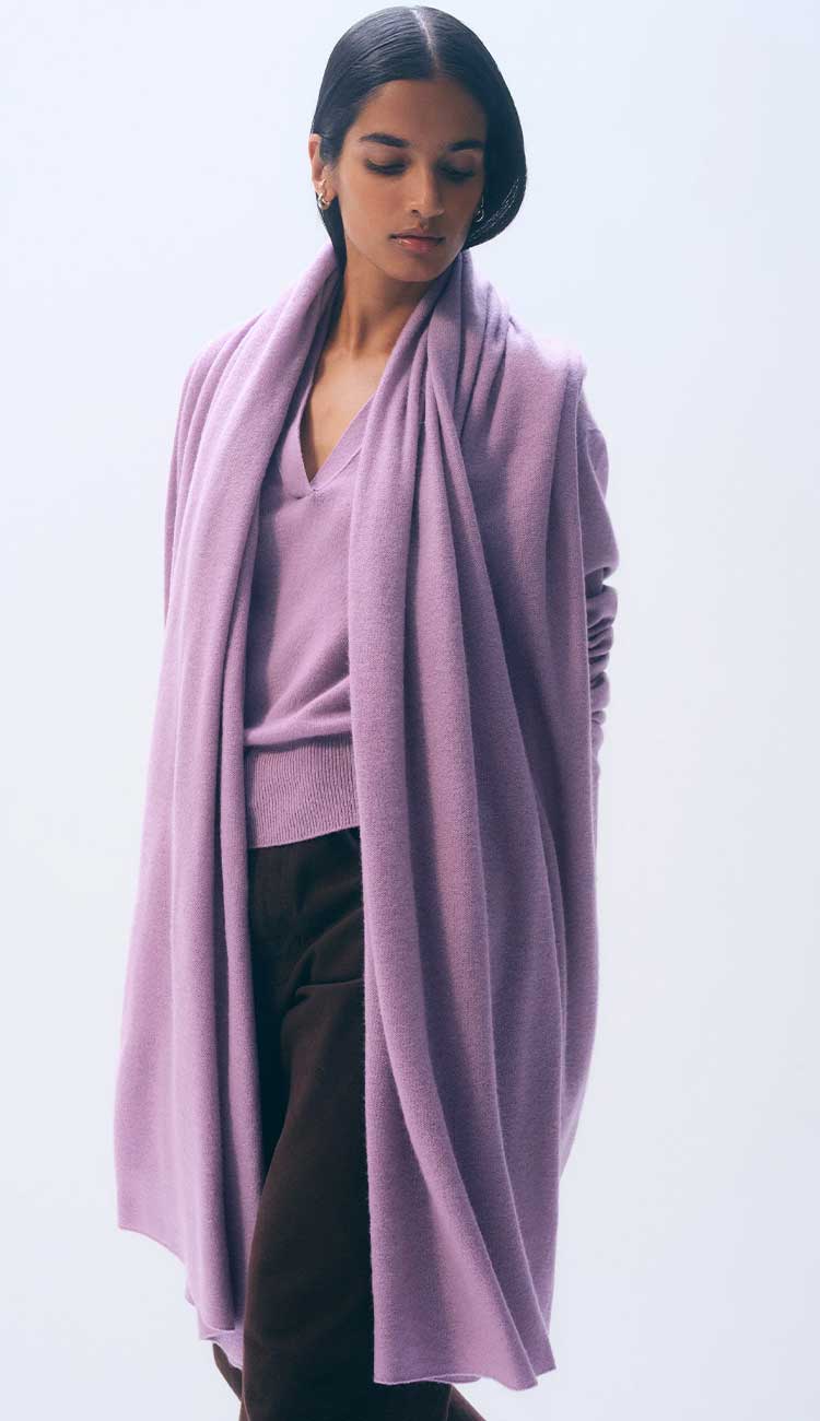 WOMAN WEARING A PLUM SCARF AND SWEATER WITH BLACK PANTS ON A GREY BACKGROUND