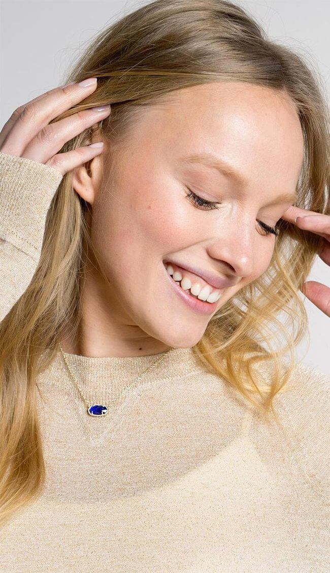 blue stone gold tone necklace kendra scott over a beige sweater