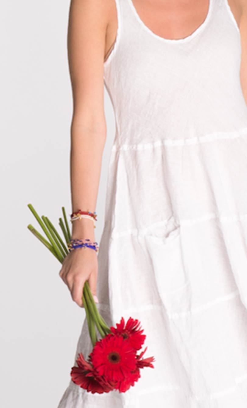 A person wearing a white dress holding a bunch of friendship bracelets with various colors.
